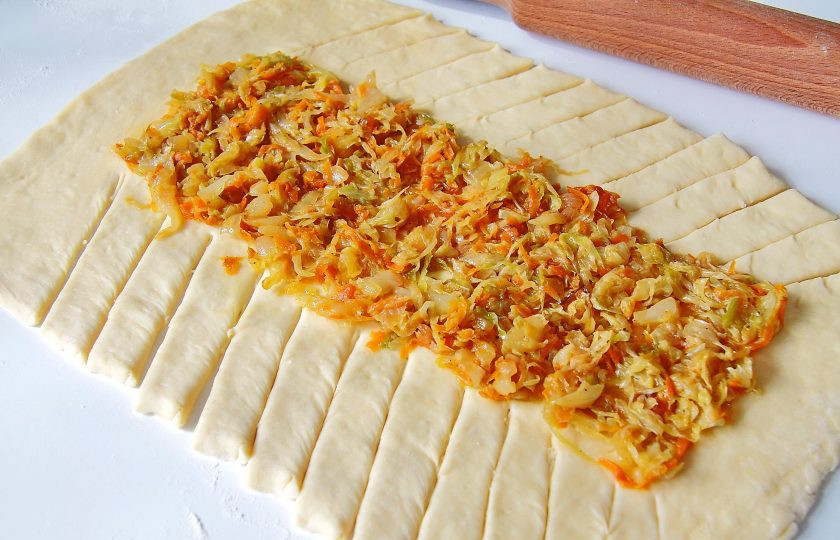 1. Этап. Кулебяка с капустой: Тесто разделите на две части. Каждую раскатайте в форме прямоугольника на присыпанной мукой поверхности. На середину положите начинку, а по бокам сделайте надрезы ножом под небольшим наклоном.