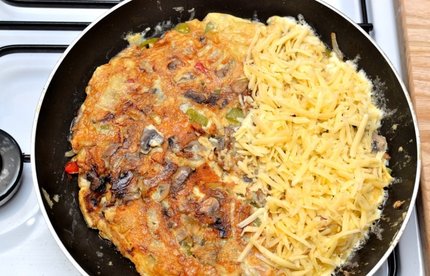 1. Этап. Омлет с сыром и овощами: Визуально разделите омлет на две половинки и на одну сторону выложите тёртый сыр.