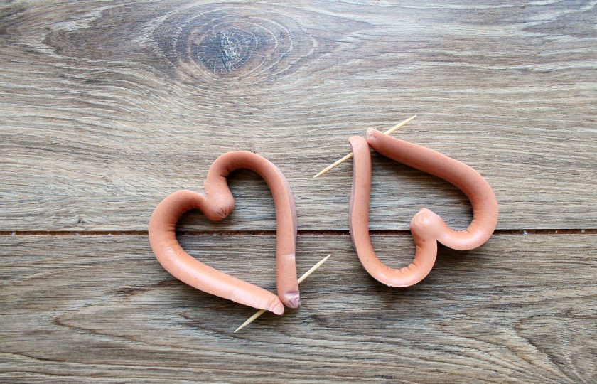 1. Этап. Яичница сердечком: Сосиски очистите от пленки, если такая имеется, и разрежьте их вдоль посередине, не доходя до другого конца примерно 2 сантиметра. Разведите концы в разные стороны и соедините, придавая сосиске форму сердца. Соедините концы зубочисткой.