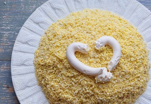 1. Этап. Салат с тунцом Новогодний шар: Яйца предварительно отварить, очистить от скорлупы. Разделить на белки и желтки. Желтки натереть на мелкой тёрке, распределить поверх крабовых палочек, смазать майонезом.