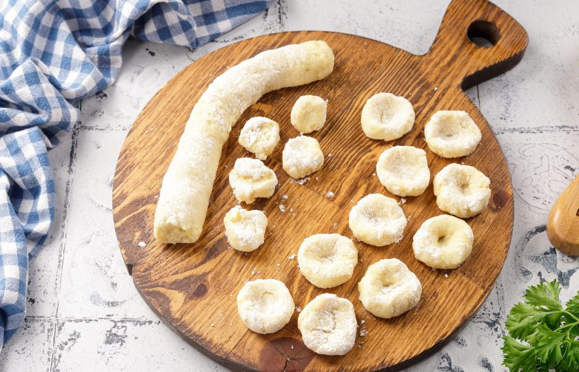 1. Этап. Картофельные клёцки с сыром: Дайте тесту полежать 15 минут, после чего нарежьте на части. Рабочую поверхность посыпьте мукой, раскатайте каждую часть в жгутики и порежьте на маленькие кусочки. Каждый кусочек обваляйте в муке, формируя маленькие лепёшки и сразу же придавите центр пальцем, для получения углубления.