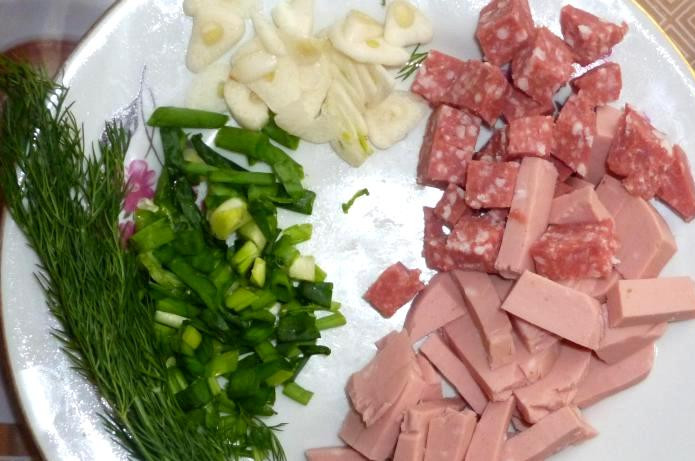 1. Этап. Омлет с колбасой: Нарезаем колбасу на небольшие кусочки, измельчаем свежую зелень, а чеснок нарезаем пластинками.