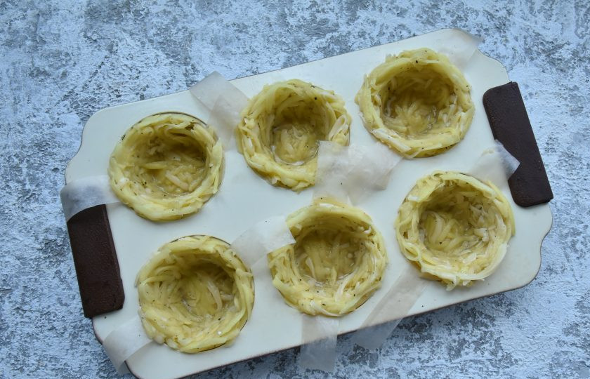 1. Этап. Картофельные корзиночки с селедочным кремом: Подготовьте формы для выпекания корзиночек. Можно использовать силиконовые формы, из них будет легче извлечь готовые корзиночки. На дно металлических форм желательно положить по кружочку из пергаментной бумаги. Разделите картофельную массу по количеству формочек. В каждую формочку выложите порцию картофеля и распределите массу по бокам и дну форм.