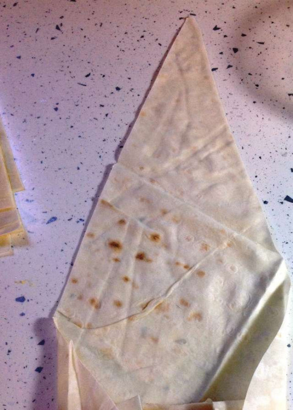 1. Этап. Сигары из лаваша: 3. На широкую часть треугольника положите немного начинки и начинайте скручивать. Сделайте пару оборотов, а затем, подвернув края лаваша внутрь, продолжайте скручивать.