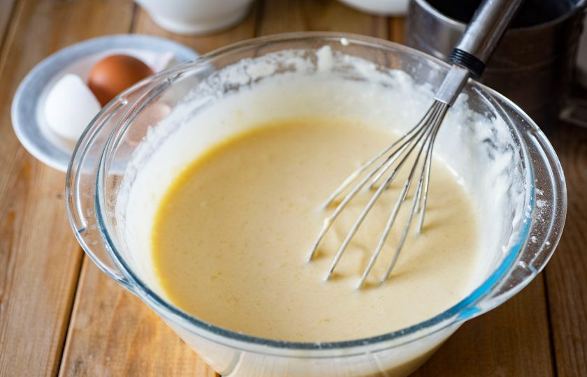 1. Этап. Кокосовый кекс на кефире: Вмешайте муку в жидкую смесь с помощью венчика до полного соединения.