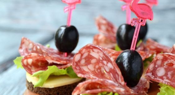 1. Этап. Канапе для праздничного стола: На сыр уложите промытые листья салата, нарезку из московской колбасы и оливку. Закрепите всё шпажками.