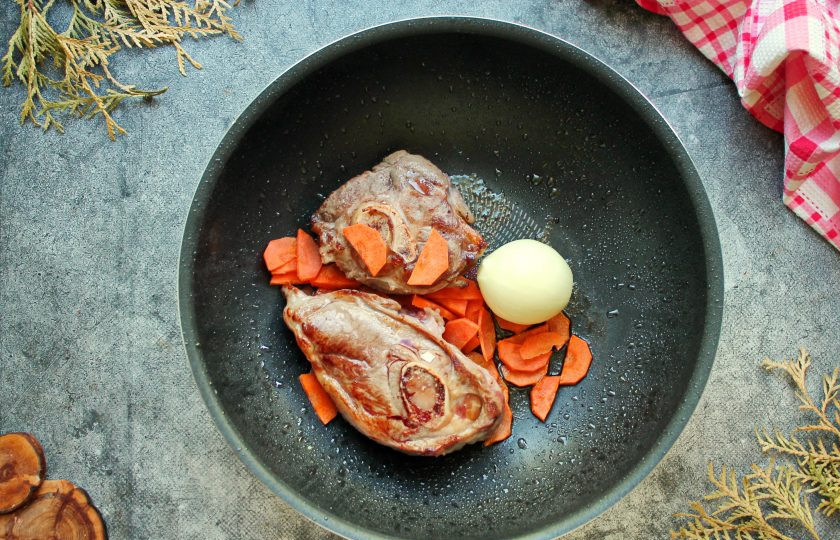 1. Этап. Суп Соуз: Убавьте огонь до среднего и добавьте к мясу одну очищенную, целую луковицу. Морковь порежьте полукольцами и добавьте в казан.