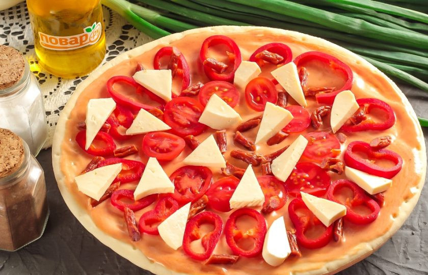 1. Этап. Болгарская пицца: Нарежьте брынзу треугольничками или средними кубиками, а копченые колбаски — ломтиками. Выложите на основу.