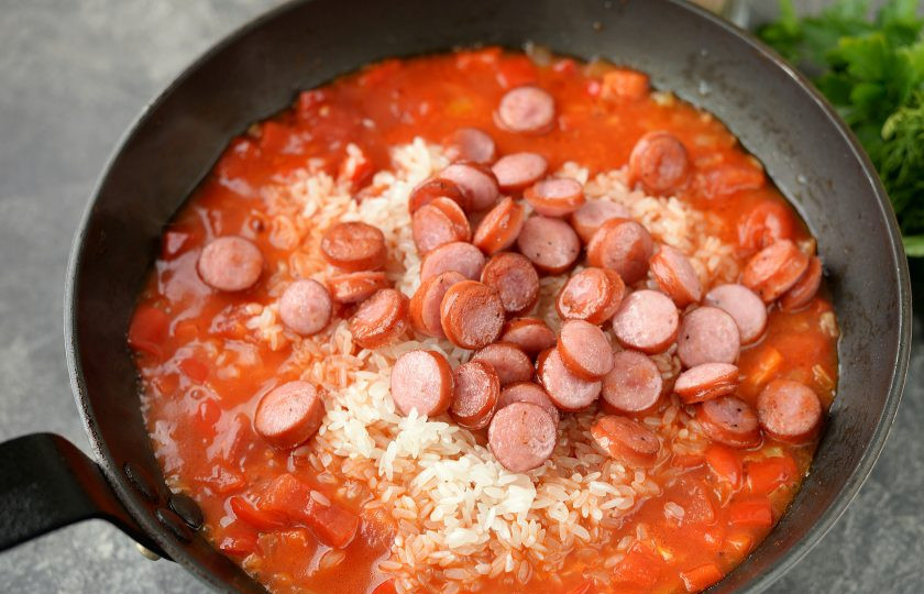 1. Этап. Американский обед: Рис тщательно промойте до чистой воды, добавьте в сковороду вместе с колбасками, перемешайте.