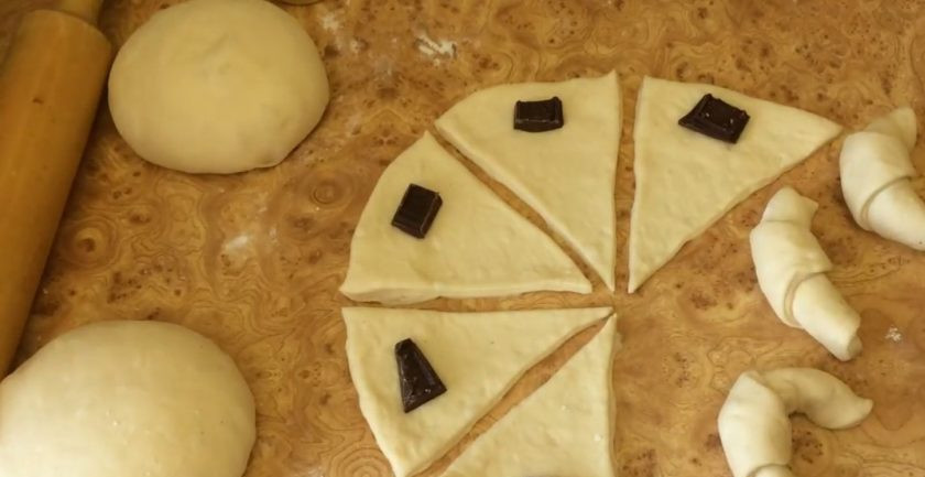 1. Этап. Рогалики с шоколадной начинкой: На основание получившихся треугольников выложите кусочки шоколада и сверните рулетом. Придайте рогаликам форму подковы. Выложите рогалики на противень, покрытый пергаментом и накройте пищевой пленкой.