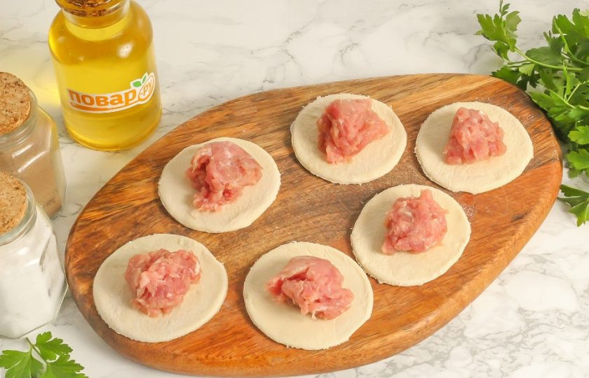 1. Этап. Пельмени Бульмени: Извлеките подмороженный фарш из морозилки и скатайте из него крупные колобки. Выложите их на кружочки теста.