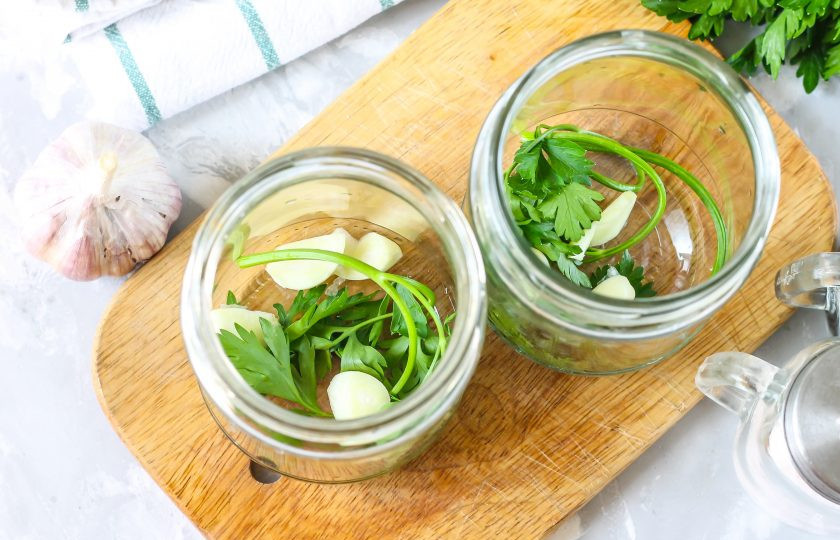 1. Этап. Помидоры с семенами горчицы на зиму: Промойте банки и крышки. Промойте свежую зелень петрушки или сельдерея, выложите на дно емкостей. Очистите от шелухи чесночные зубчики, добавьте по две штуки в каждую банку.