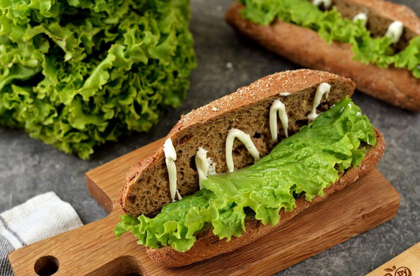 1. Этап. Бутерброд с солеными огурцами: Разрежьте лист латука на две части, выложите на одну сторону булки.