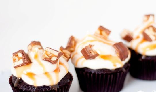 1. Этап. Капкейки со Сникерсом и карамельной глазурью: 4. Полить капкейки глазурью. Украсить каждый капкейк 4-5 кусочками Сникерса и полить карамельным соусом.