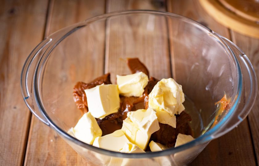 1. Этап. Торт Муравейник с медом: Приготовьте крем. В просторную миску выложите всю вареную сгущенку, добавьте жидкий мед и 180 грамм сливочного масла. Миксером взбивайте эти ингредиенты до получения однородного крема.