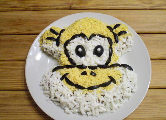 1. Этап. Салат Обезьянка: Белком и желтком выложите отдельные зоны обезьяньей мордочки. Оливками подчеркните рельеф, оформите глазки. Обезьянка готова!