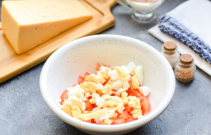1. Этап. Салат с помидорами и курицей: Куриное яйцо почистите и нарежьте небольшими кубиками, добавьте в салатник.