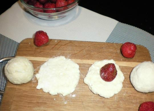 1. Этап. Творожные кнедлики с клубникой: 5. Клубнику хорошо промойте или разморозьте и удалите влагу. Из теста сформируйте небольшие толстенькие лепешки, в центр которых поместите по ягодке клубники, бока поднимите в верх и закрепите. В итоге у вас должен получиться небольшой шарик, главное чтобы он был не тоненьким, а то в процессе варки может развалиться.