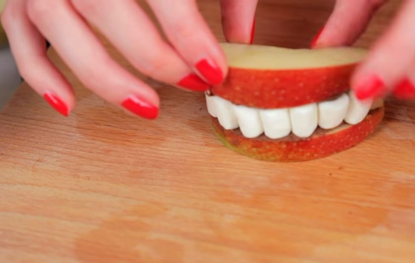 1. Этап. Снеки к Хэллоуину: 3. Далее приготовьте диетические челюсти. Для этого разрежьте яблоко и возьмите две дольки. Смажьте их нутеллой и выложите на одну половинку маршмеллоу в форме зубов. Затем прикройте такие челюсти второй долькой яблока.