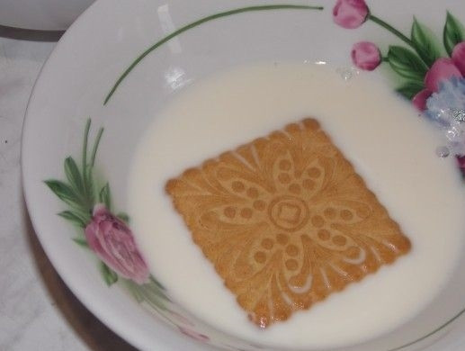 1. Этап. Торт Домик без выпечки: 1. На столе расстелите пищевую пленку или пергамент. Подогрейте слегка молоко и каждое печенье на несколько секунд окуните в него, затем выложите в 3 ряда, в каждом по 5 штук.