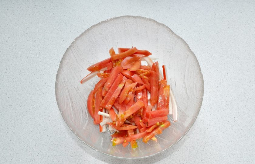 1. Этап. Салат Крабовое море: Тонкими ломтиками нарежьте помидор.