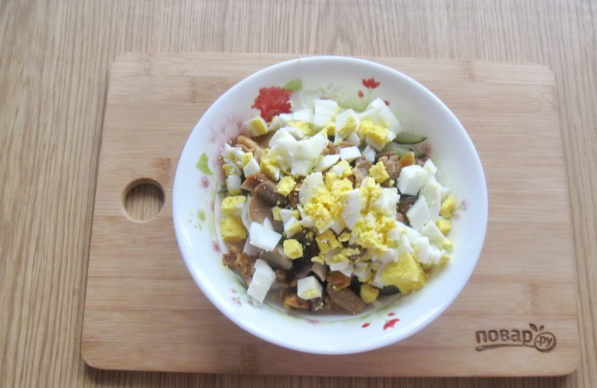 1. Этап. Салат с ветчиной и маринованными грибами: Яйца сварите вкрутую, охладите, очистите и нарежьте. Выложите в салатник.