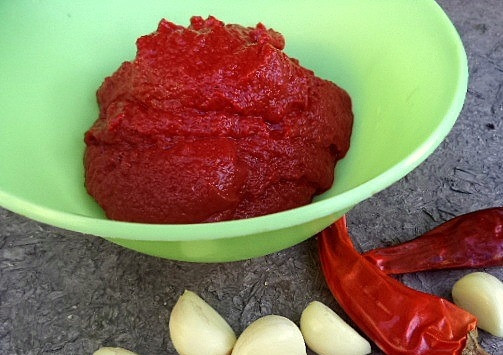 1. Этап. Аджика из томатной пасты: Чесночок очистите от шелухи. Острый перчик вымойте и обсушите. Перекрутите ингредиенты в мясорубке или измельчите их острым ножом. Если хотите, чтобы аджика получилась более острой, то не очищайте жгучий перец от семян. Добавьте подготовленные ингредиенты вместе с томатной пастой к измельченным сливам и перцу.