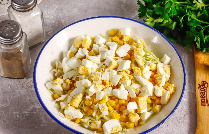 1. Этап. Салат из капусты с кукурузой и яйцом: Очистите отварные куриные яйца от скорлупы и промойте в воде. Нарежьте кубиками и добавьте в емкость.