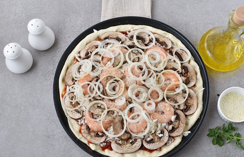 1. Этап. Пицца с креветками и грибами: На сыр выложите нарезанные ломтиками грибы и очищенные креветки. Посыпьте луком, слегка присолите и поперчите по вкусу. Посыпьте отложенной моцареллой поверх всего. Сбрызните оливковым маслом по вкусу.