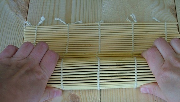 1. Этап. Роллы с тунцом консервированным: 4. Сворачивайте при помощи бамбукового коврика в плотную колбаску. Процесс начинайте с той стороны, где лежат ингредиенты. Свободную часть смочите водой и закрепите к получившемуся рулету.