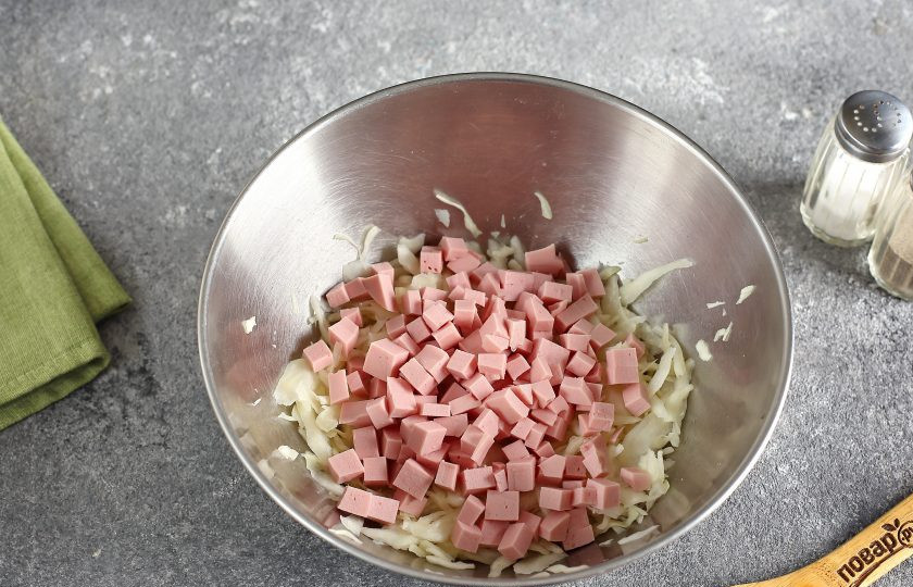 1. Этап. Салат с яйцом, капустой и колбасой: Добавьте нарезанную кубиками колбасу.