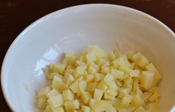 1. Этап. Салат с крабовыми палочками, яйцом и майонезом: Картофель вымойте и поместите в кастрюлю. Залейте его водой и отварите до готовности. Остудите картофель, очистите его от кожуры. Нарежьте кубиками и выложите в миску.