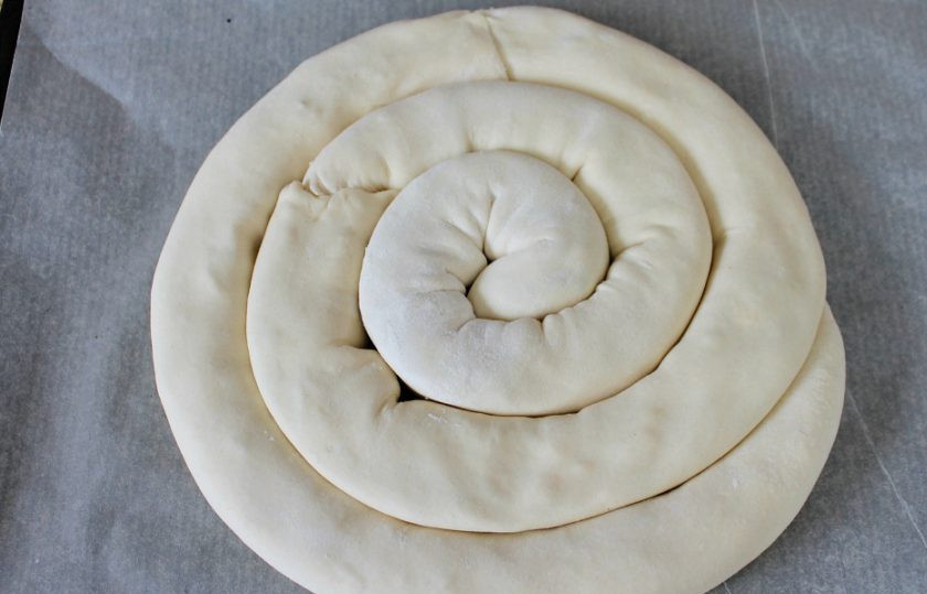 1. Этап. Греческая улитка: На противень покрытый пекарской бумагой выкладываем рулеты из теста в виде улитки. Края соединяем и защипываем тесто. Край улитки подворачиваем под низ пирога.