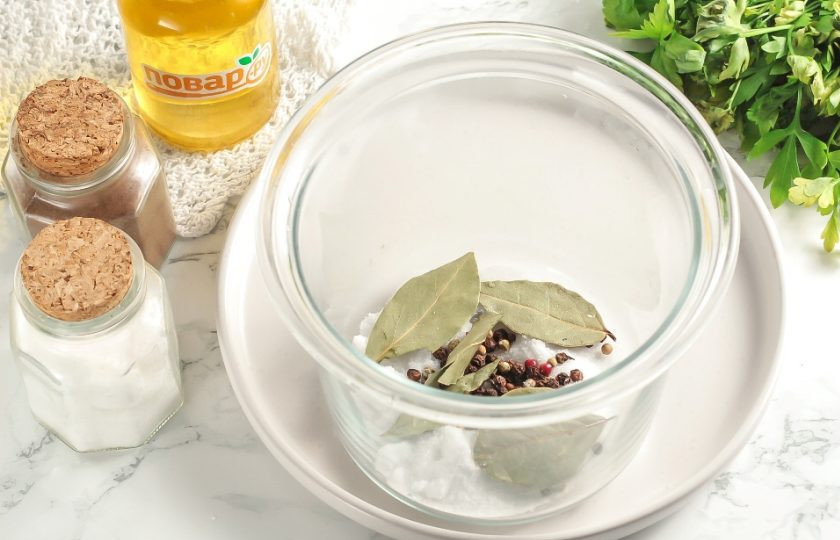 1. Этап. Бекон в домашних условиях: Подготовьте необходимые ингредиенты для приготовления домашнего бекона в кухонных условиях. В глубокую узкую емкость всыпьте соль, горошины черного перца и лавровые листья.