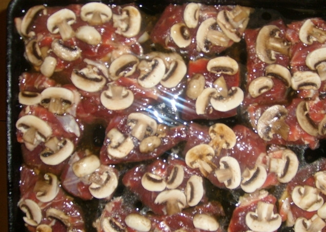 1. Этап. Говядина по-французски в духовке: На кусочки мяса выкладываем нарезанные грибы.