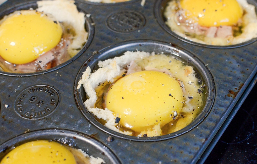 1. Этап. Маффины с яйцом на завтрак: 4. Натрите сыр, а сверху разбейте яйцо. Приправьте его солью и перцем.