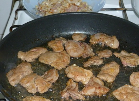 1. Этап. Куриная печень в сметане: Удалите лук со сковороды в отдельную посуду. На том же масле обжарьте в несколько заходов печень с двух сторон, примерно по 1 минуте на каждую сторону.