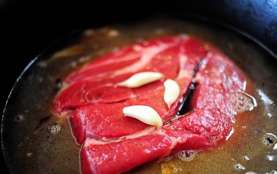 1. Этап. Говядина тушеная с соевым соусом: 2. Выложить говядину поверх лука. Добавить зубчики чеснока, соевый соус, херес, соль, воду, розмарин, тимьян и другие специи на ваше усмотрение. Накрыть кастрюлю крышкой и варить на медленном огне в течение 6 часов, пока говядина не станет нежной, и мясо не будет легко отделяться от костей.