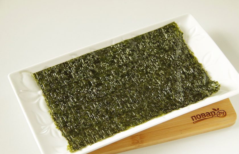 1. Этап. Салат Суши: Листы нори вырежьте кухонными ножницами по размеру блюда, на котором будете подавать салат. Это может быть круглое или прямоугольное, если будете подавать на квадратной тарелке, то листы можно оставить целыми, но тогда количество ингредиентов возможно уйдет чуть больше. Положите первым лист нори шероховатой стороной вверх.