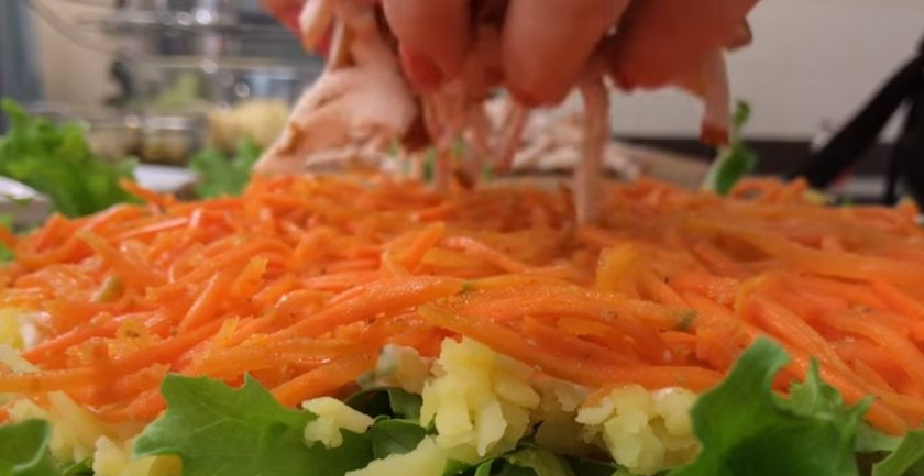 1. Этап. Сытный салат Золотой петушок: 2. Отварной картофель натрите на крупной терке сразу на листья салата. Смажьте его сметаной с майонезом, сверху выложите морковь по-корейски.