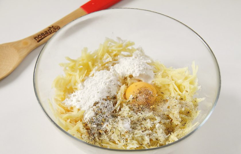 1. Этап. Картофельная запеканка на сковороде: Для основы запеканки натрите на крупной терке картофель. Добавьте к нему измельченный чеснок, муку, яйцо, соль и специи по вкусу.