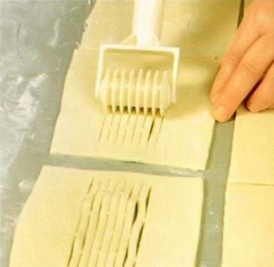 1. Этап. Слойки с лимоном: 2. Размороженное тесто раскатываем толщиной 5 миллиметров, разрезаем его на квадраты размером примерно 15х15 сантиметров. Специальным или обычным кухонным ножом делаем надрезы в центре половины всех квадратов.