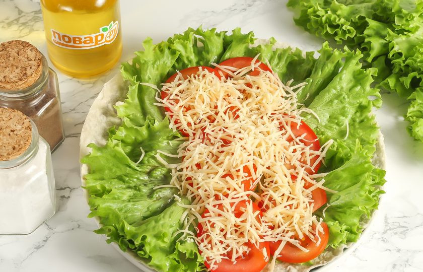 1. Этап. Цезарь ролл с наггетсами: Промойте помидоры и вырежьте зеленые сердцевинки. Нарежьте кружочками и выложите на салат. Натрите твердый сыр на терке с мелкими ячейками.