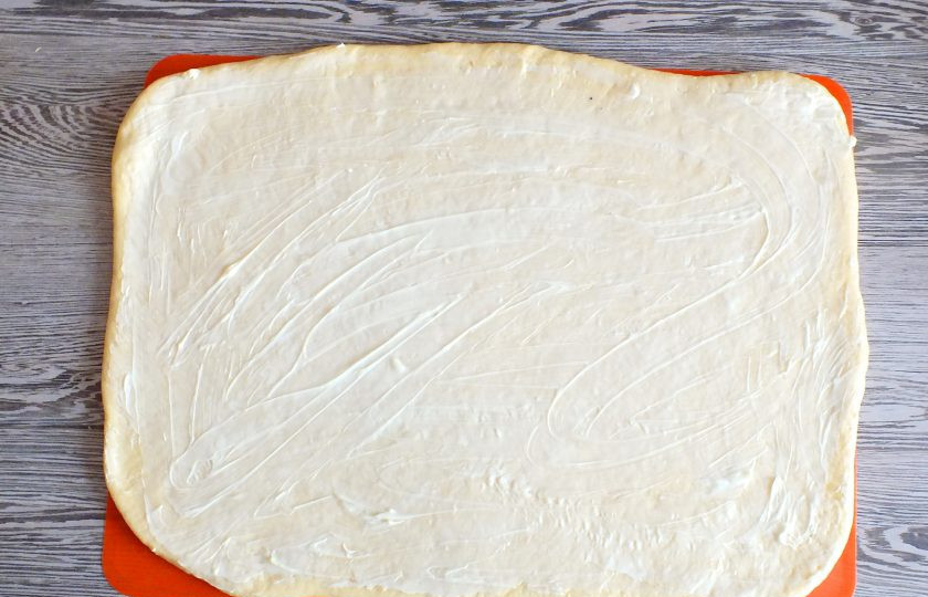 1. Этап. Синнабоны с малиной: На рабочей поверхности раскатайте пласт толщиной 0,3 см. Смажьте его мягким сливочным маслом (40 грамм).