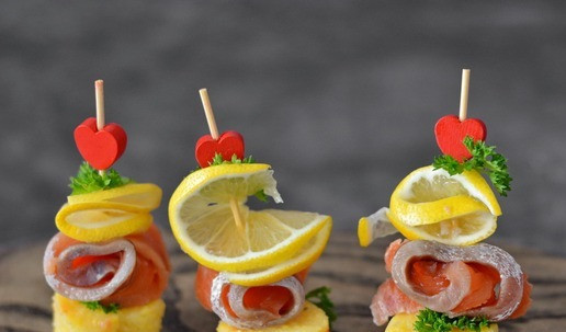 1. Этап. Канапе с лососем на кукукрузной поленте: Соберите канапе: на шпажку нанизывайте свёрнутый ломтик лимона, затем рулетик из слабосоленого лосося и воткните шпажку в основание из поленты. Украсьте петрушкой.