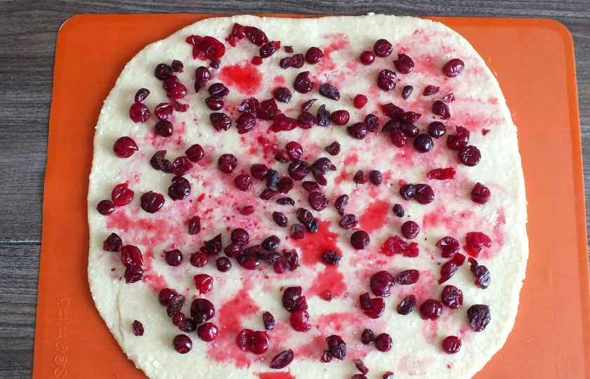 1. Этап. Творожный рулет с клюквой: Раскатайте тесто в пласт толщиной 0,3 см. С начинки слейте выделившийся сок и выложите на пласт. Сверху посыпьте вяленой клюквой.