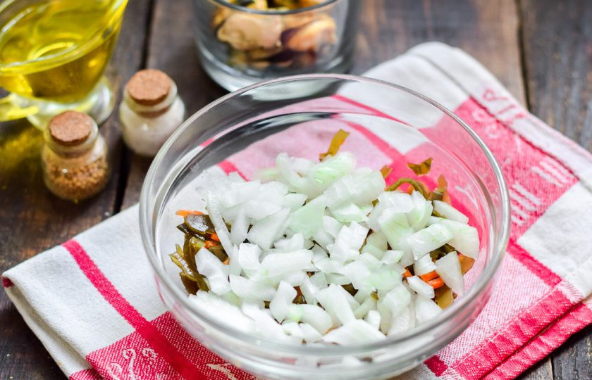 1. Этап. Салат с мидиями и морской капустой: Очистите репчатый лук, сполосните и просушите. Нарежьте лук небольшими кубиками и добавьте к капусте. Так как сама капуста маринованная, лук заберет в себя часть вкусовых ноток и станет менее ядреный.
