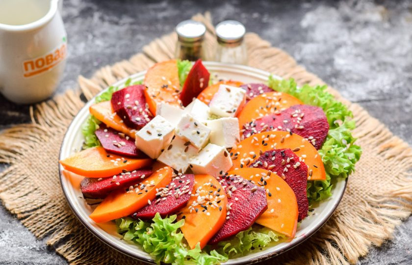 1. Этап. Салат с хурмой и свеклой: В центр салата выложите нарезанный кубиками сыр, сбрызните все маслом, добавьте соль и перец по вкусу. По желанию посыпьте кунжутом.