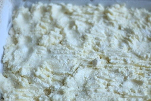 1. Этап. Детская творожная запеканка в духовке: 3. На дно формы положите бумагу для выпечки. На нее ровным слоем выложите половину крошки. Сверху положите творог, разровняйте.