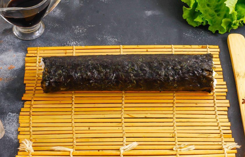 1. Этап. Роллы с курицей и ананасом: Смочите незаполненный край нори водой и аккуратно сверните в рулет, слегка прижимая начинку, чтобы роллы получились плотными.